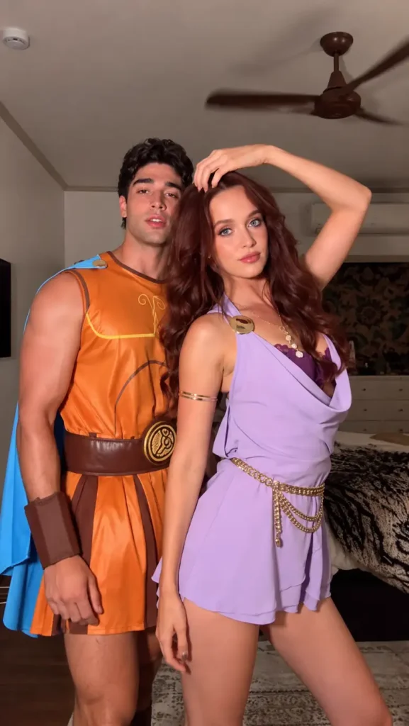 Couple dressed as Hercules and Megara in orange, blue, lavender, and gold Halloween costumes.