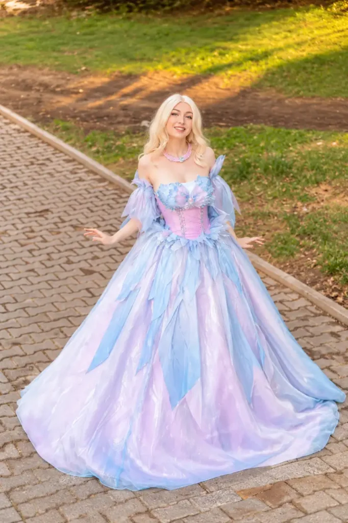 Woman wearing a pastel blue and lavender fairy princess gown with pink corset bodice, petal details, sheer sleeves, and full flowing skirt.