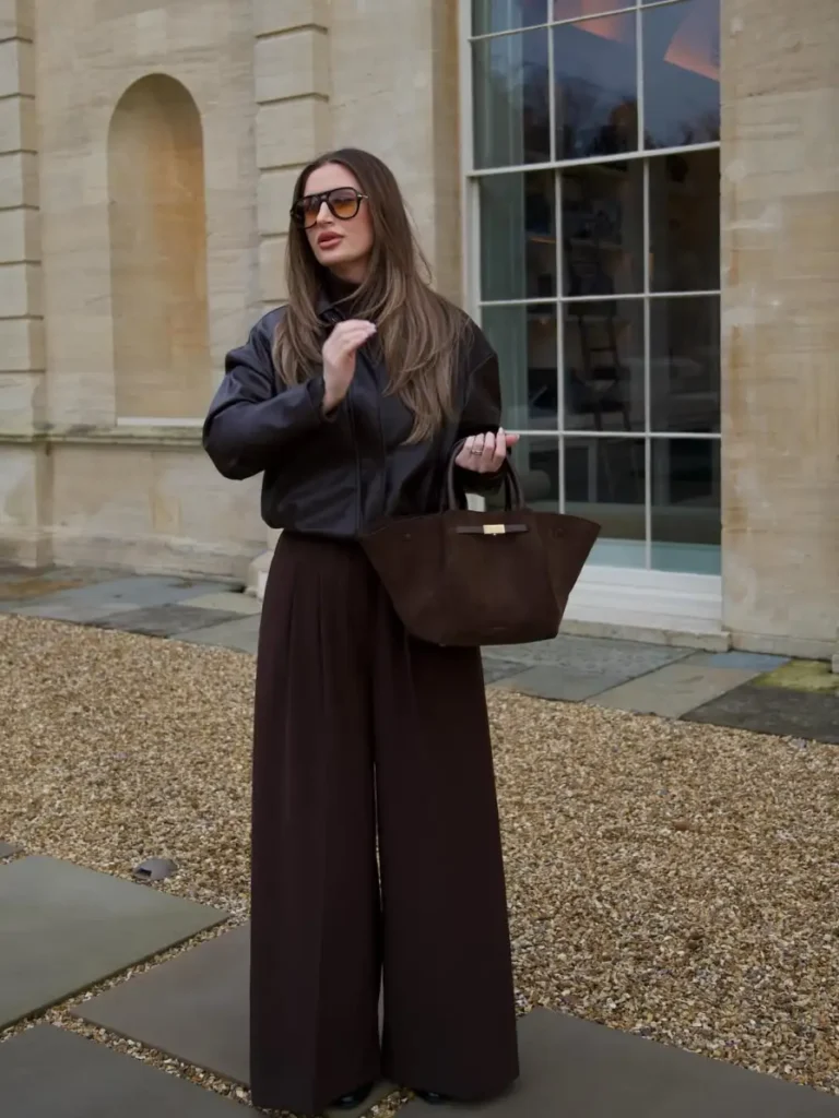 Woman wearing a dark chocolate leather jacket with matching extra-wide trousers, oversized sunglasses, and a brown tote for a monochrome fall outfit.