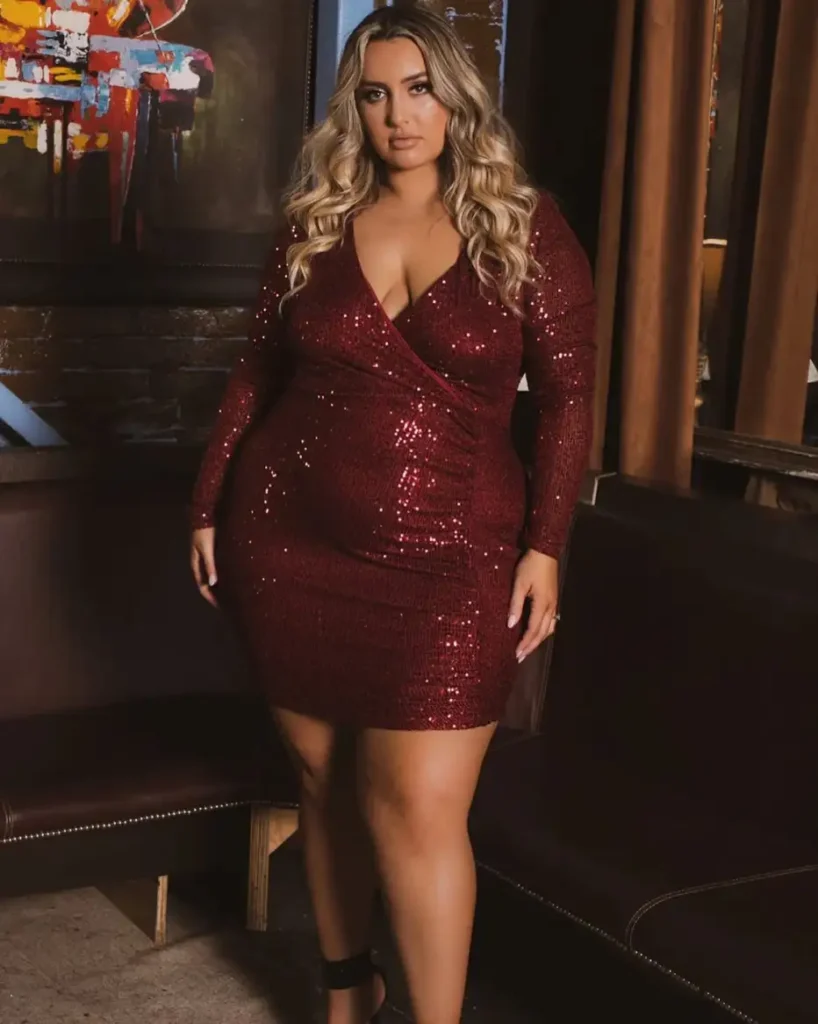 Plus size woman wearing a deep burgundy long-sleeve sequin wrap mini dress for a glamorous fall date night or evening outfit.