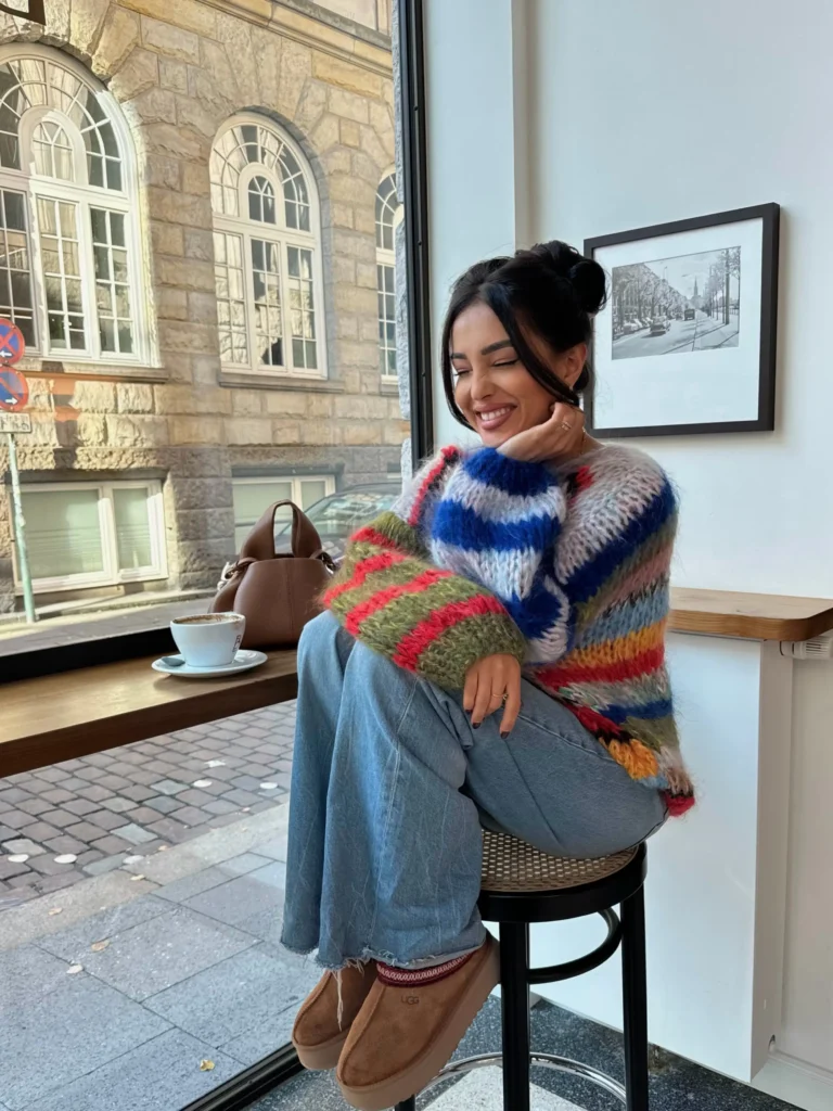 Colorful striped chunky sweater styled with relaxed wide-leg jeans, brown suede shoes, and a brown handbag for a casual fall outfit.