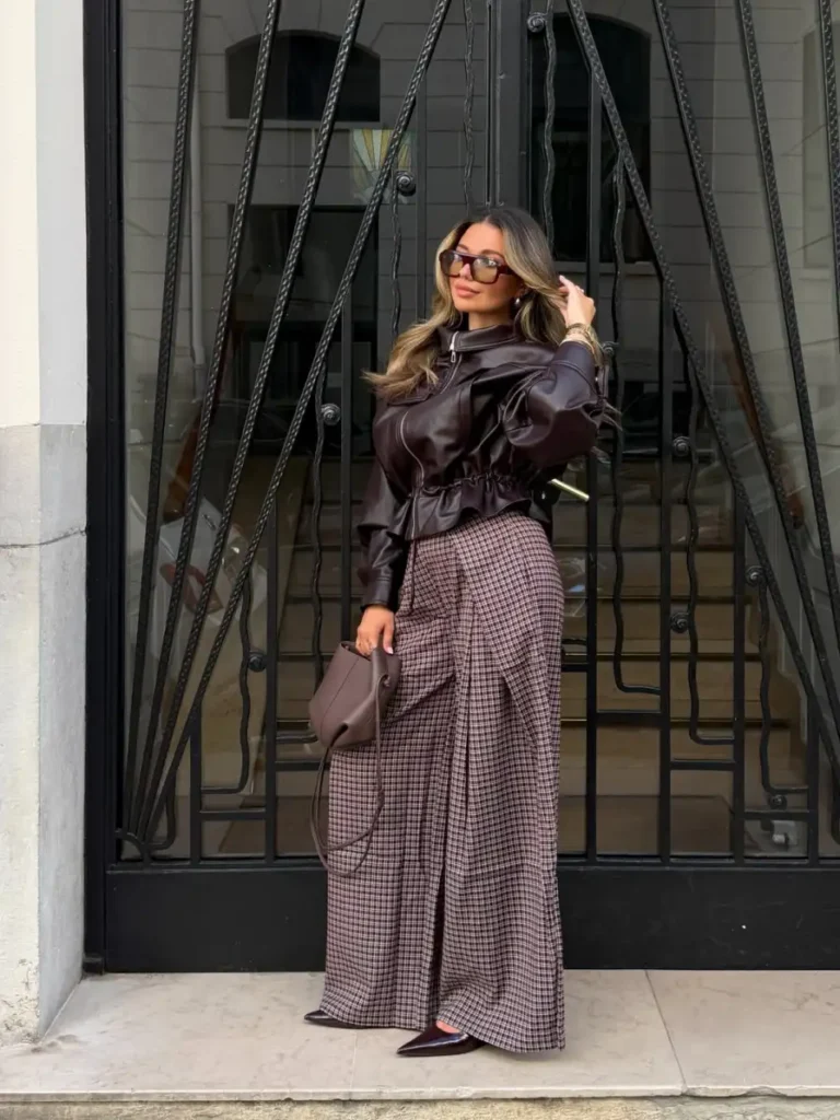 Woman wearing a dark chocolate leather jacket with brown plaid wide-leg trousers, pointed burgundy shoes, and a taupe handbag for a chic fall outfit.