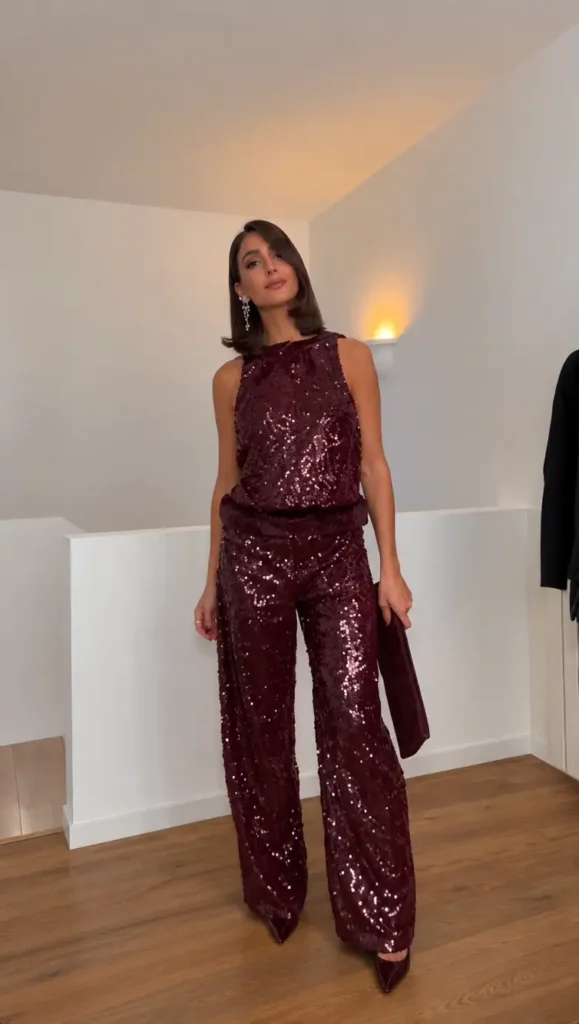 Woman wearing a matching burgundy sequin sleeveless top and wide-leg trousers with pointed burgundy heels, sparkling earrings, and a matching clutch for Christmas.