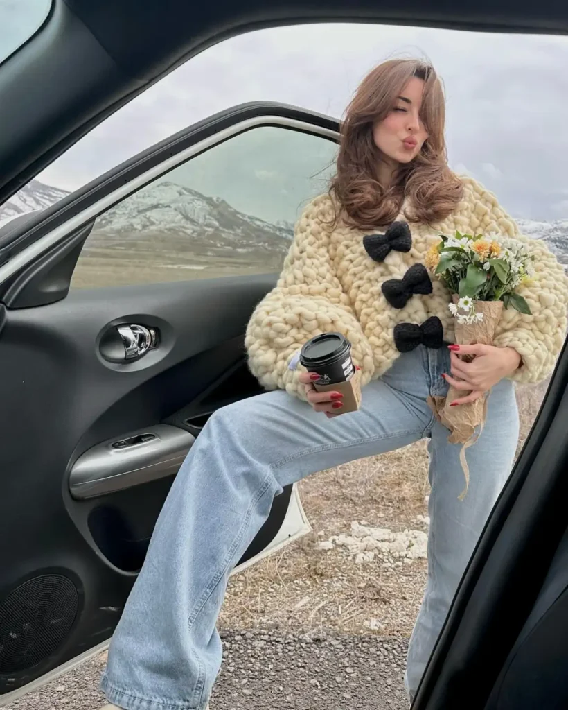 Woman wearing a chunky cream knitted cardigan with oversized black bow closures and relaxed light-wash wide-leg jeans for a cute, trendy winter outfit.