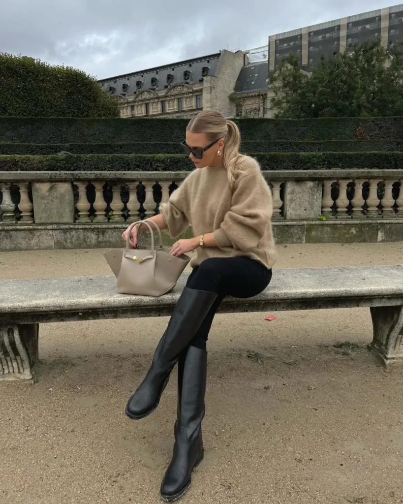 Oversized beige sweater paired with slim black pants, tall black leather boots, and a taupe handbag for a chic fall outfit.
