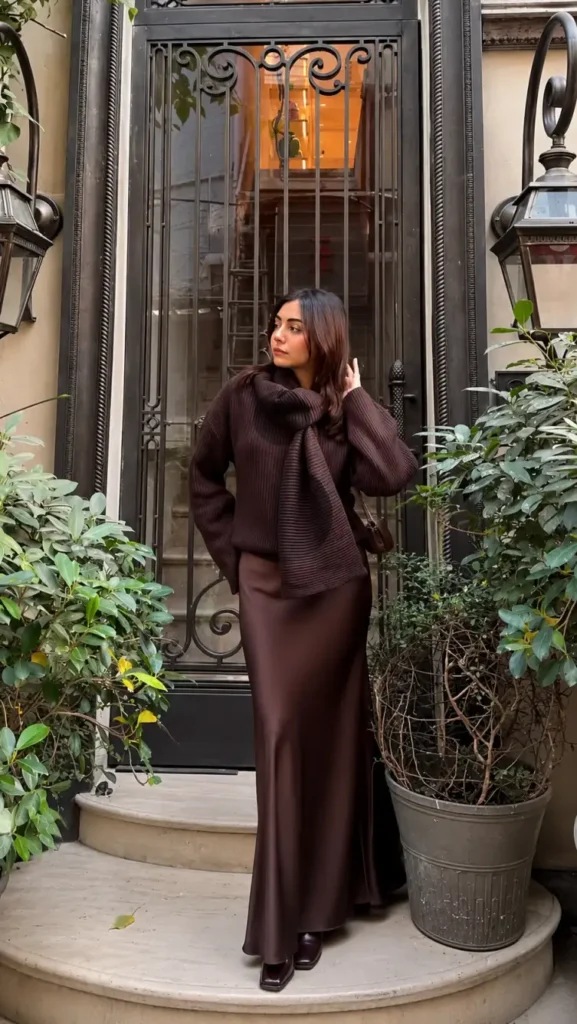 Woman wearing a chocolate-brown ribbed sweater with a matching draped knit scarf, silky brown satin maxi skirt, and dark square-toe boots for an elegant monochrome winter outfit.