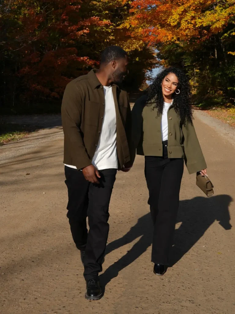 Couple wearing casual Thanksgiving outfits with olive utility jackets, white shirts, black trousers, and coordinating earthy fall colors.