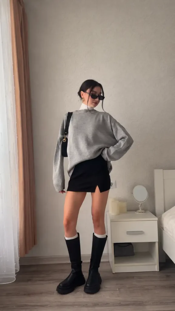 Gray oversized sweater styled with black mini skirt, white turtleneck, knee-high boots, and white socks.