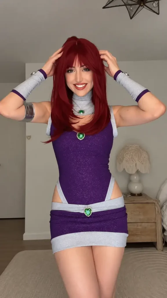Woman wearing a sparkly purple superhero costume with silver trim, green gem details, red hair, and metallic arm accessories.