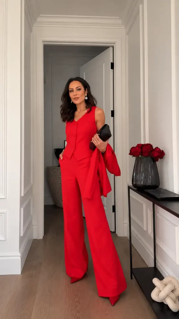 Woman wearing a bright red tailored waistcoat with matching wide-leg trousers, red pointed heels, and a black clutch for an elegant New Years Eve dinner outfit.