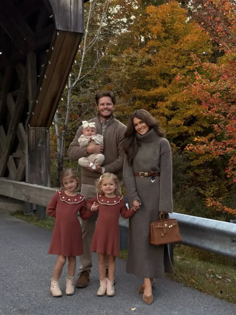 Family wearing coordinated autumn outfits with Mom in a belted taupe sweater dress, Dad in a brown cardigan, two girls in matching rust knit dresses, and baby in cream.