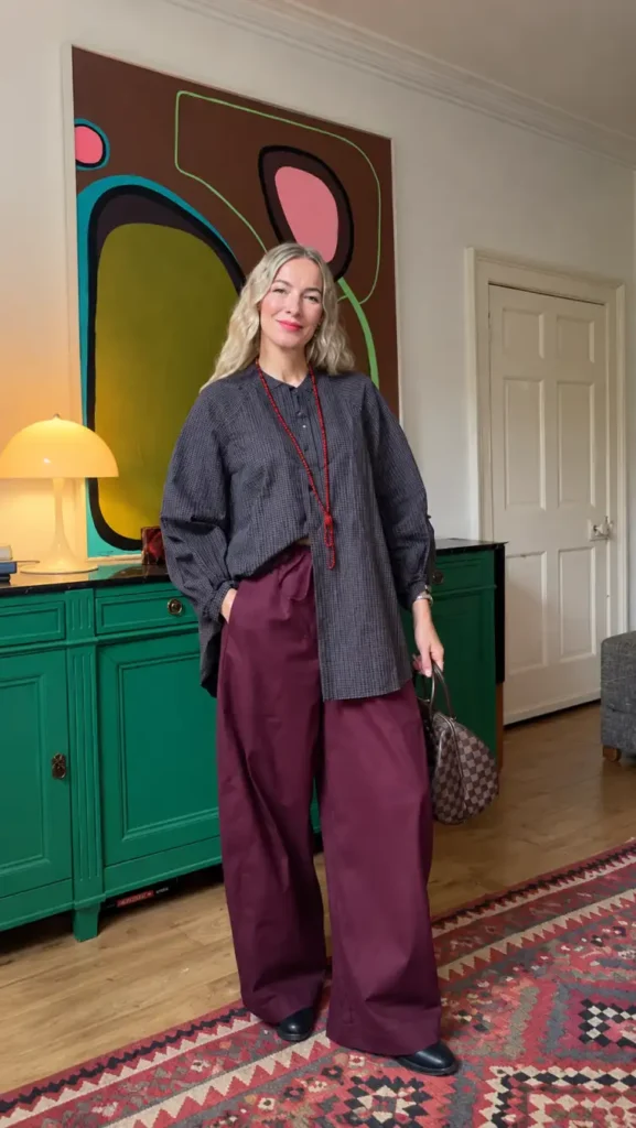 Woman over 50 styling an oversized charcoal button-down shirt with burgundy wide-leg trousers, a long red necklace, and black shoes for a modern casual Thanksgiving look.