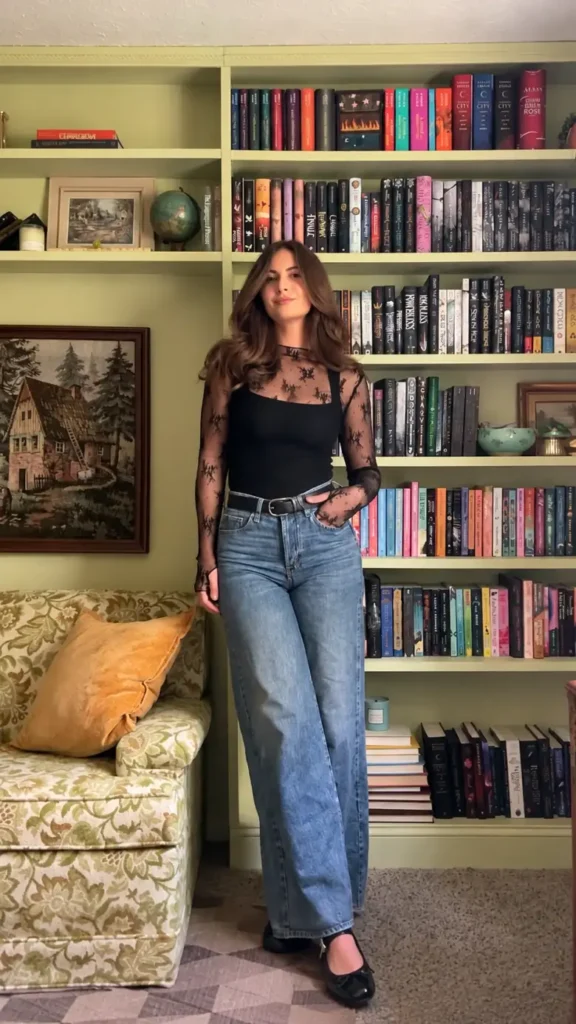 Woman wearing a black sheer lace top over a fitted black camisole with blue wide-leg jeans, black belt, and flats.