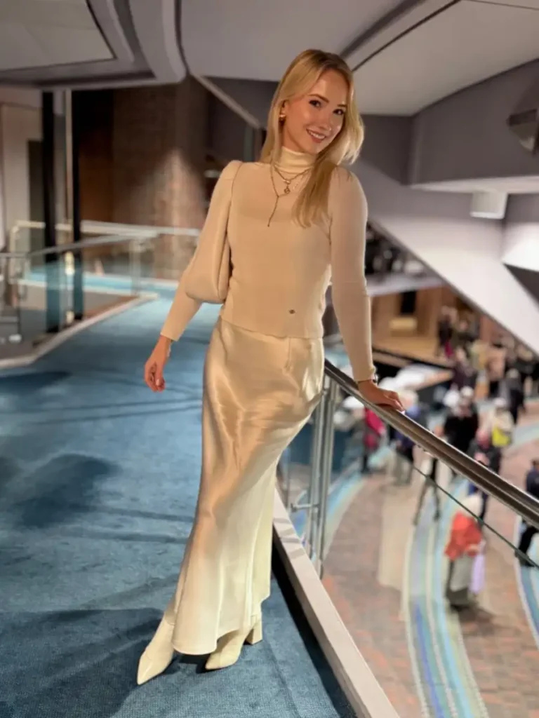 Beige turtleneck sweater styled with a champagne satin maxi skirt, cream pointed boots, and layered gold necklaces.
