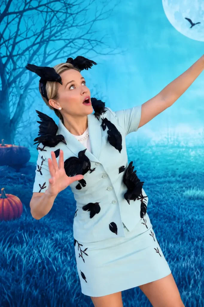 Woman wearing a pale blue skirt suit covered with black birds and feathers for a creative spooky bird attack Halloween costume.