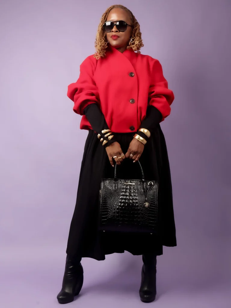 Black woman wearing a bright red cropped jacket over a black midi skirt with tall black boots, gold bracelets, and a structured handbag for a bold fall outfit.