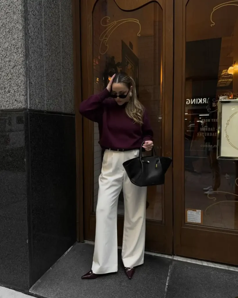 Woman wearing a burgundy sweater with cream wide-leg trousers, burgundy pointed shoes, and a structured black tote for a polished fall look.