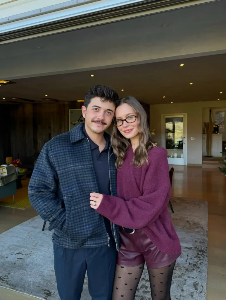 Couple wearing stylish fall outfits with a burgundy oversized sweater, leather-look shorts, heart-print tights, and a navy checked jacket for Friendsgiving.