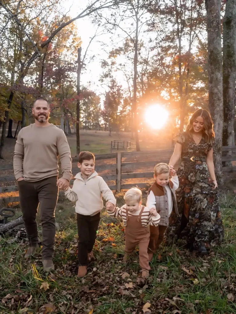 Family wearing earth tone fall outfits with Mom in a dark floral maxi dress, Dad in a taupe sweater, and three boys in cream, brown plaid, striped knitwear, and rust overalls.