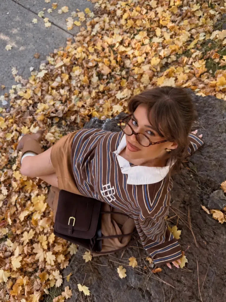 Brown striped sweater layered over a white collared shirt with camel mini skirt and brown handbag.