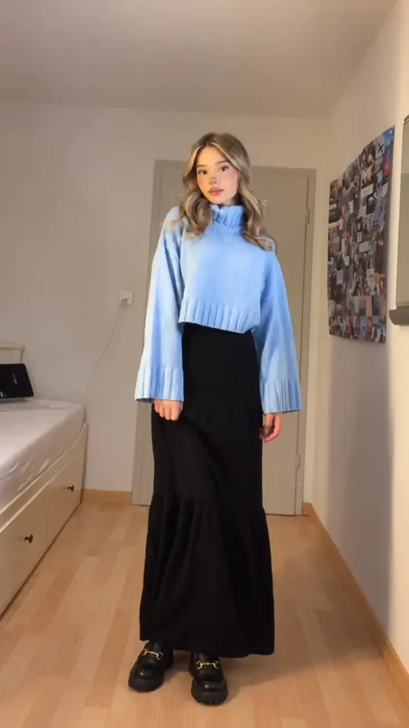 School girl wearing a cropped baby-blue turtleneck sweater with a long black tiered maxi skirt and chunky black loafers with gold buckles for a cozy school outfit.