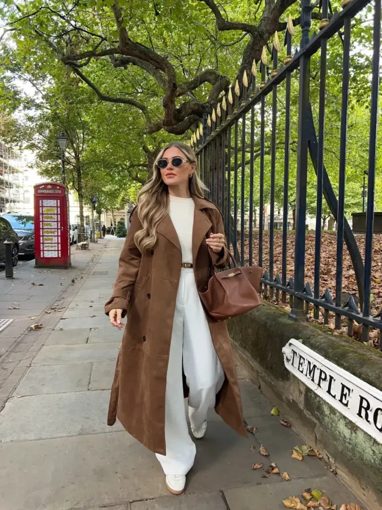 Long brown coat styled with a cream top, white wide-leg trousers, loafers, sunglasses, and a brown handbag for polished fall fashion.