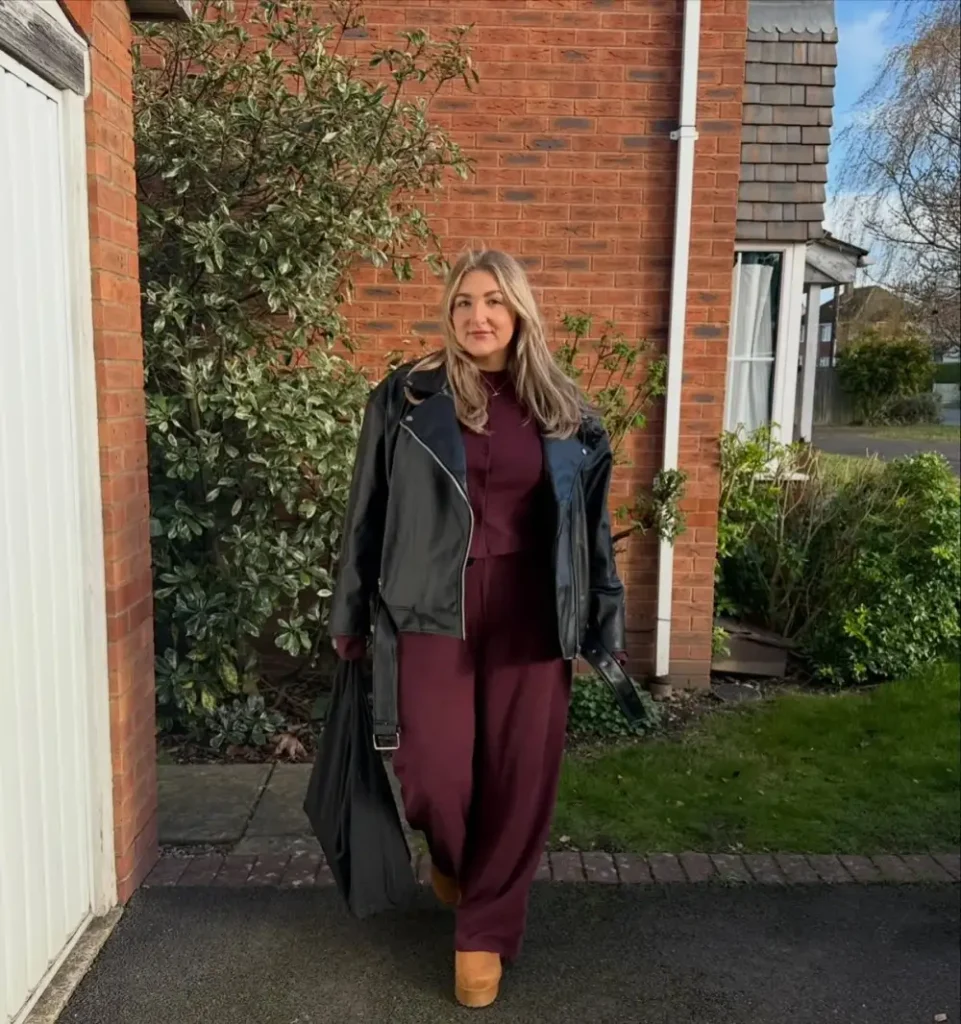 Plus size fall outfit with a burgundy cardigan and wide-leg pants layered under a black leather biker jacket with tan platform shoes.
