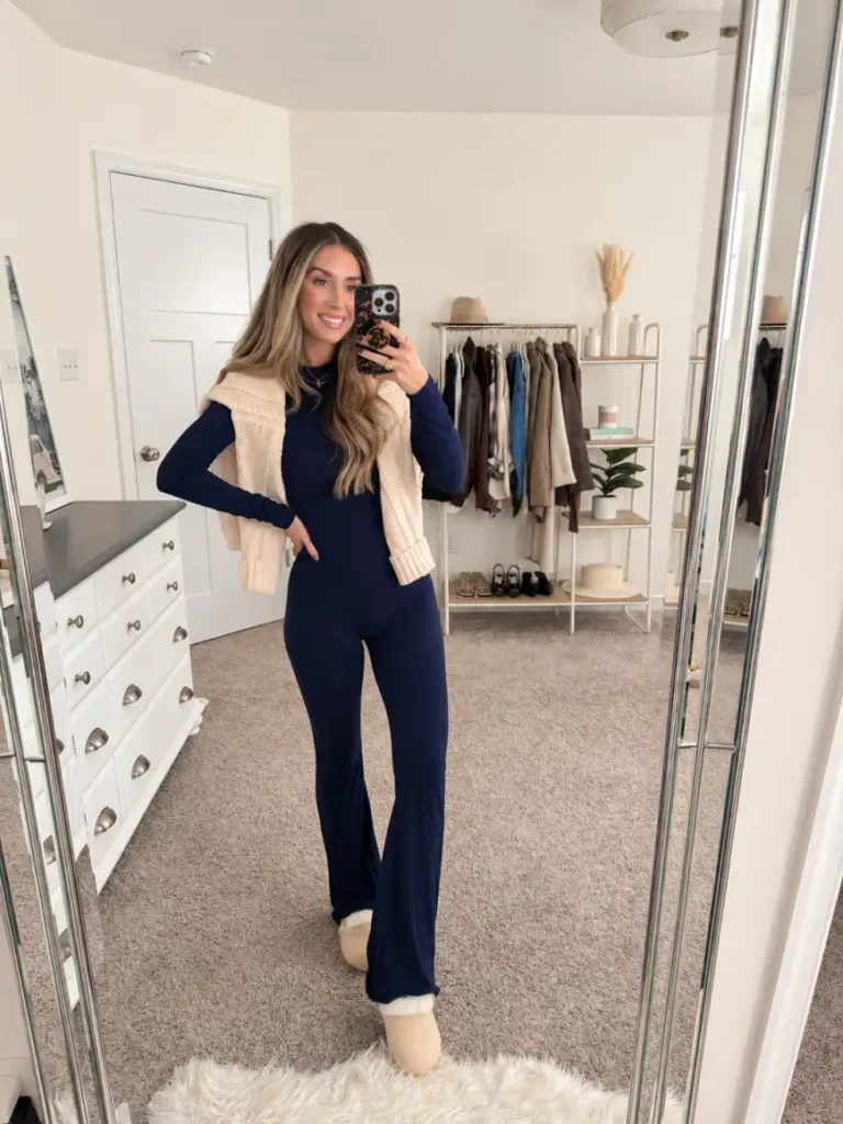 Woman wearing a navy matching lounge set with flared pants, a cream cable-knit layer over her shoulders, and cozy slippers for a casual Friendsgiving night at home.