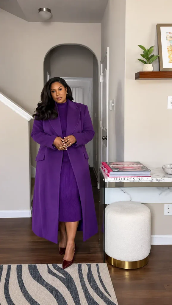 Plus size Black woman wearing a purple ribbed sweater dress with a matching long purple coat and burgundy pointed heels for an elegant fall fashion look.