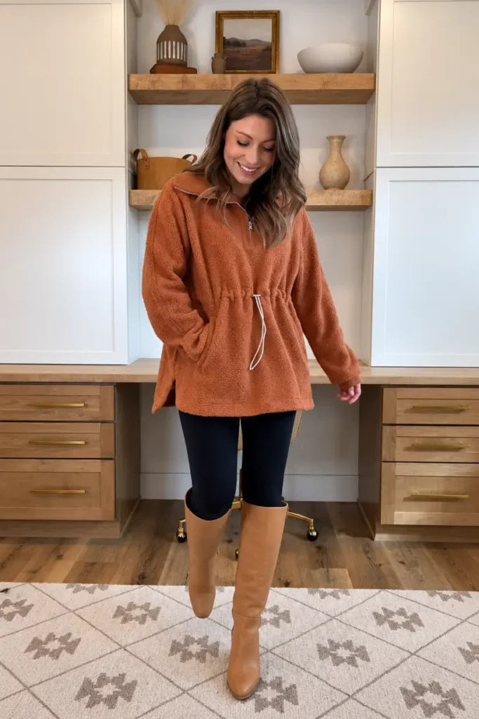 Woman wearing a rust orange fleece quarter-zip pullover with a drawstring waist, black leggings, and tan knee-high boots for a warm and casual Thanksgiving outfit.