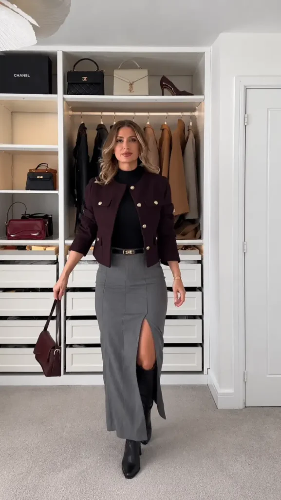 Burgundy cropped jacket with a black turtleneck, gray long skirt, knee-high black boots, and matching burgundy handbag.