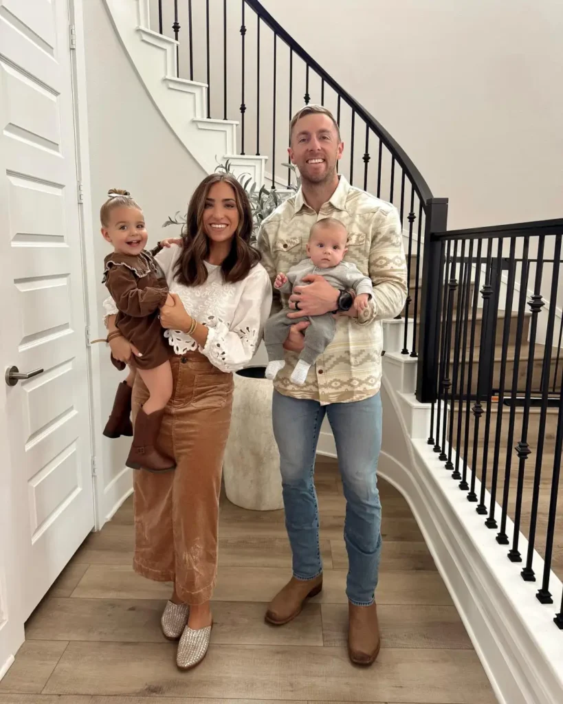 Family wearing casual Thanksgiving outfits with Mom in a brown corduroy skirt and white blouse, Dad in a patterned cream jacket and jeans, a toddler in brown, and baby in gray.