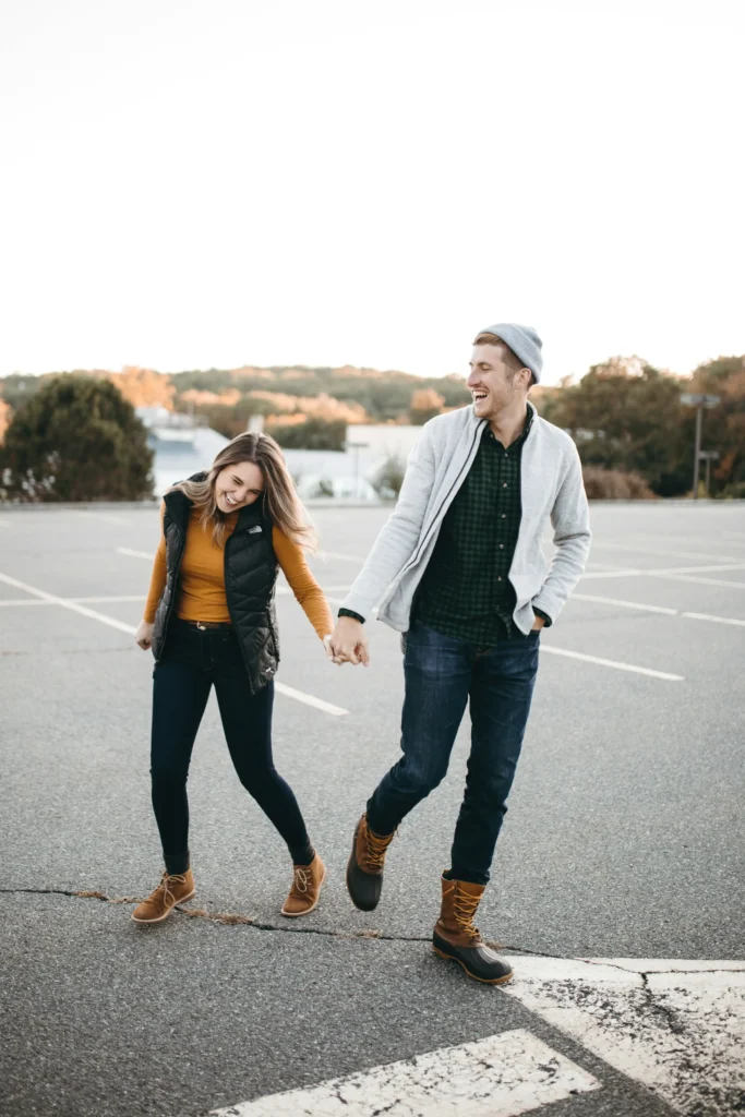 Couple wearing casual fall outfits with a mustard long-sleeve top, black puffer vest, gray jacket, plaid shirt, jeans, and brown lace-up boots.