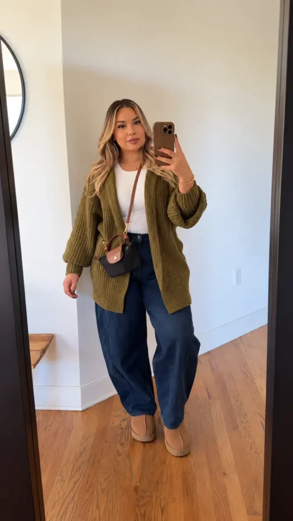 Woman wearing an oversized olive green knitted cardigan over a white top with dark blue barrel-leg jeans, tan ankle boots, and a crossbody bag for a cozy fall outfit.