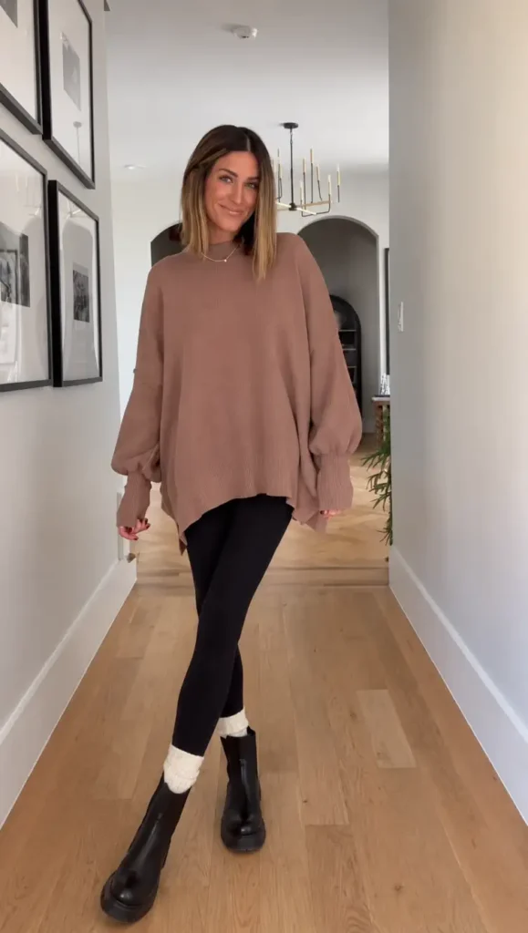 Woman wearing an oversized dusty mauve sweater with black leggings, cream socks, and chunky black ankle boots for a cozy casual Thanksgiving outfit.