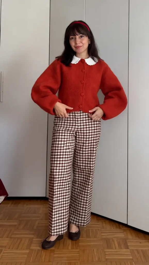 Petite woman wearing a red-orange cropped cardigan with a white Peter Pan collar, brown gingham wide-leg pants, and brown ballet flats.