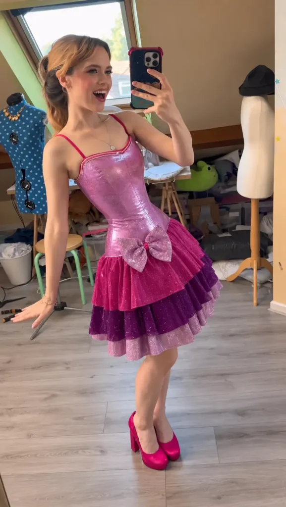 Woman wearing a sparkly pink doll-inspired mini dress with structured bodice, oversized glitter bow, layered skirt, and matching pink heels.