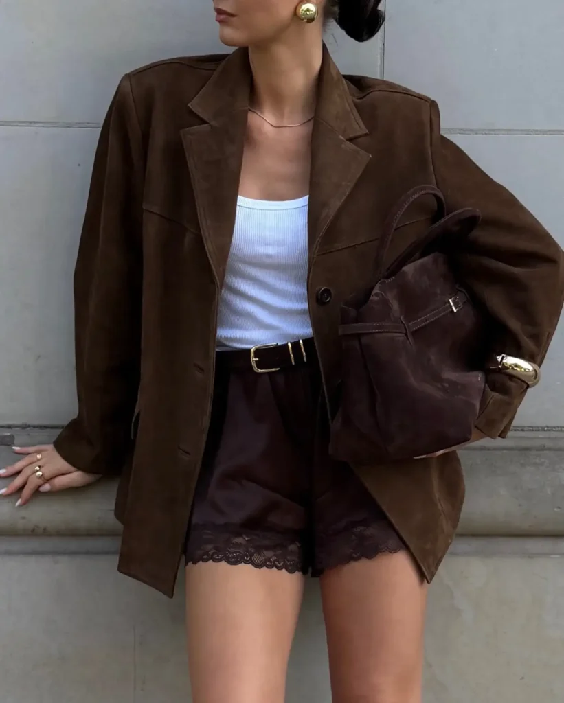Woman wearing an oversized brown blazer with a white tank, dark brown lace-trim shorts, gold jewelry, and a brown bag.