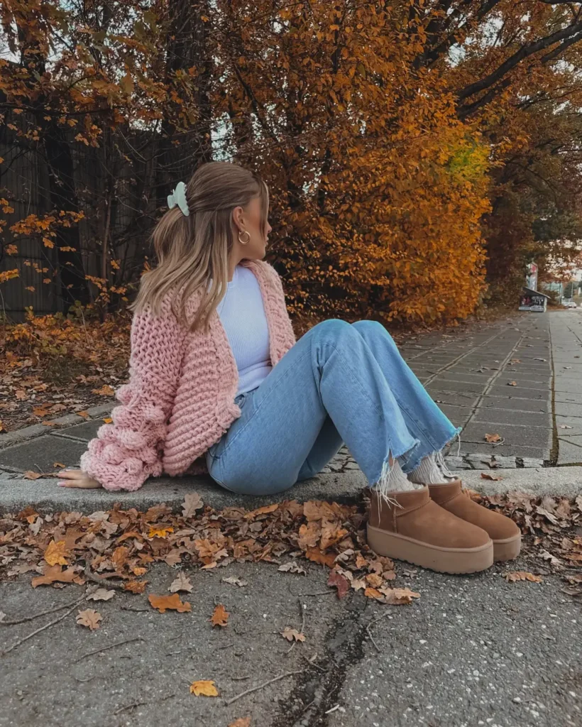 Woman wearing a chunky pink cardigan with a white top, light-wash jeans, and tan platform ankle boots for a cozy casual fall outfit.