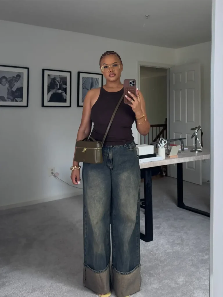 Plus size Black woman wearing a dark sleeveless top with oversized cuffed wide-leg jeans and a structured crossbody bag for casual fall style.