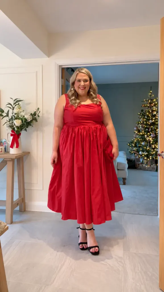 Plus-size woman wearing a bright red sleeveless fit-and-flare midi dress with a square neckline and black ankle-strap heels for a classic Christmas party look.