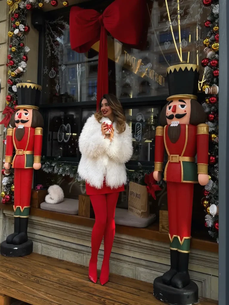 Woman wearing a bright red mini dress with matching red tights, pointed heels, and an oversized white faux fur jacket for a festive Christmas street style look.