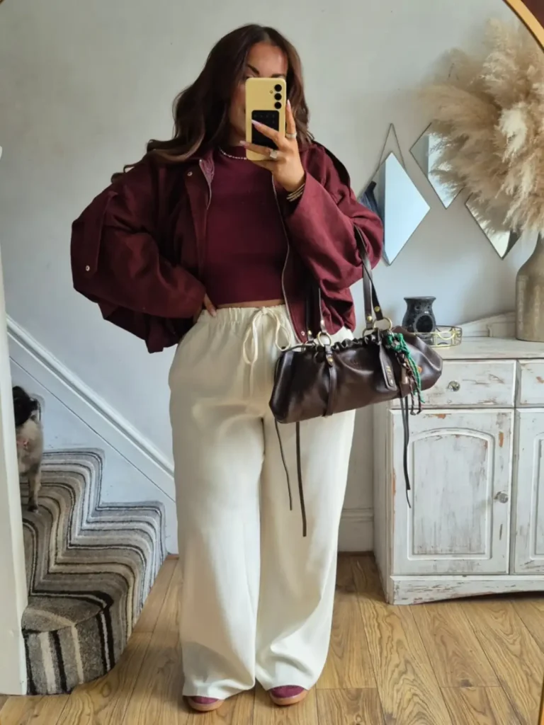 Plus size fall outfit with a burgundy jacket and matching top, cream wide-leg pants, burgundy shoes, and a dark brown shoulder bag.