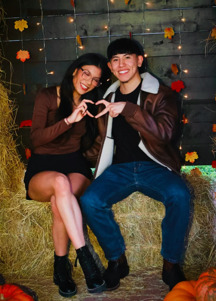 Couple wearing a chocolate-brown fitted top, black mini skirt, lace-up boots, brown shearling-collar jacket, black T-shirt, and blue jeans at a fall festival.