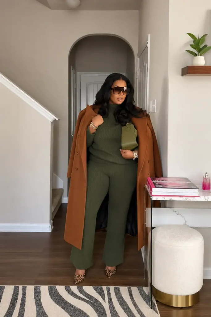 Black woman wearing an olive green ribbed knit matching set with a long caramel brown coat, leopard-print heels, and a green handbag for chic fall workwear.