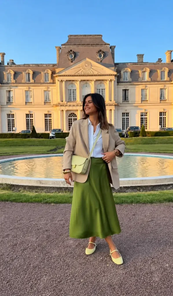 Petite woman wearing a beige blazer over a white shirt with an olive green satin midi skirt, light green Mary Jane shoes, and matching bag.