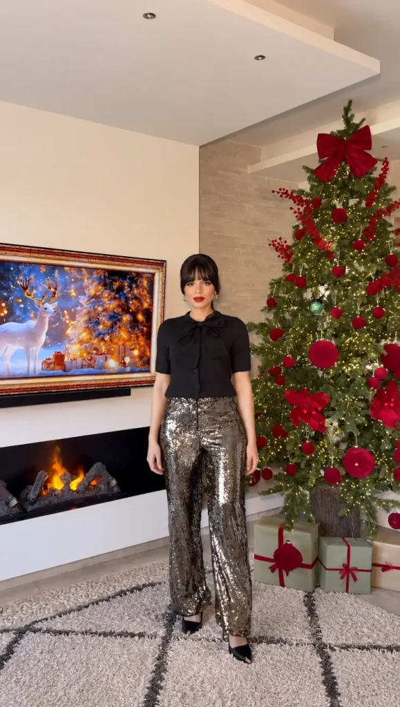 Woman styling pewter sequin wide-leg trousers with a black short-sleeve bow-neck cardigan and black pointed heels for a classy yet sparkly New Years Eve dinner outfit.