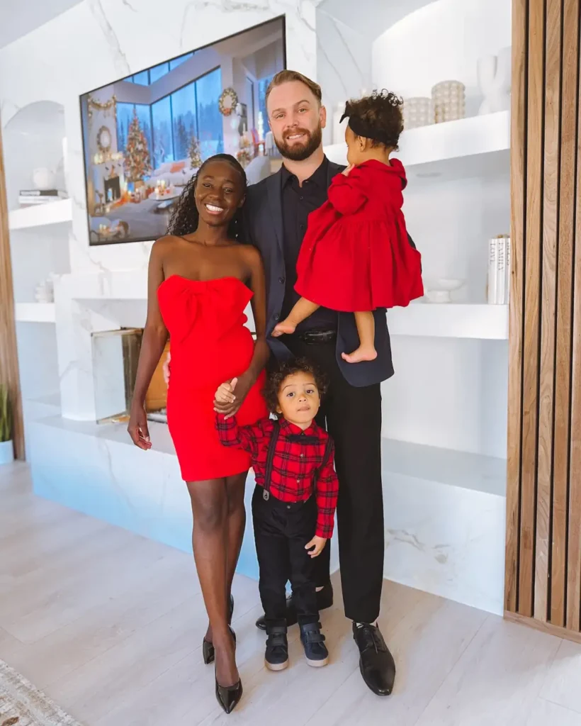 Family wearing dressy red and black outfits with Mom in a strapless red bow dress, Dad in a navy suit, a daughter in a red dress, and a son in a red plaid shirt with suspenders.