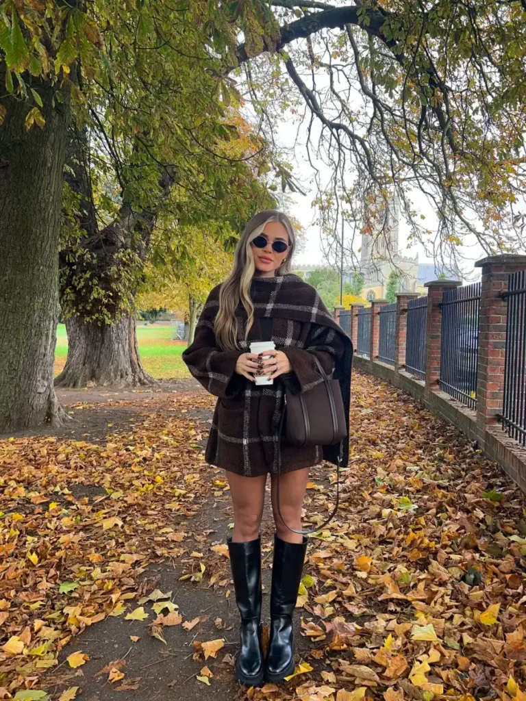 Dark brown plaid poncho styled with black knee-high boots, sunglasses, and a brown handbag for a cozy autumn outfit idea.