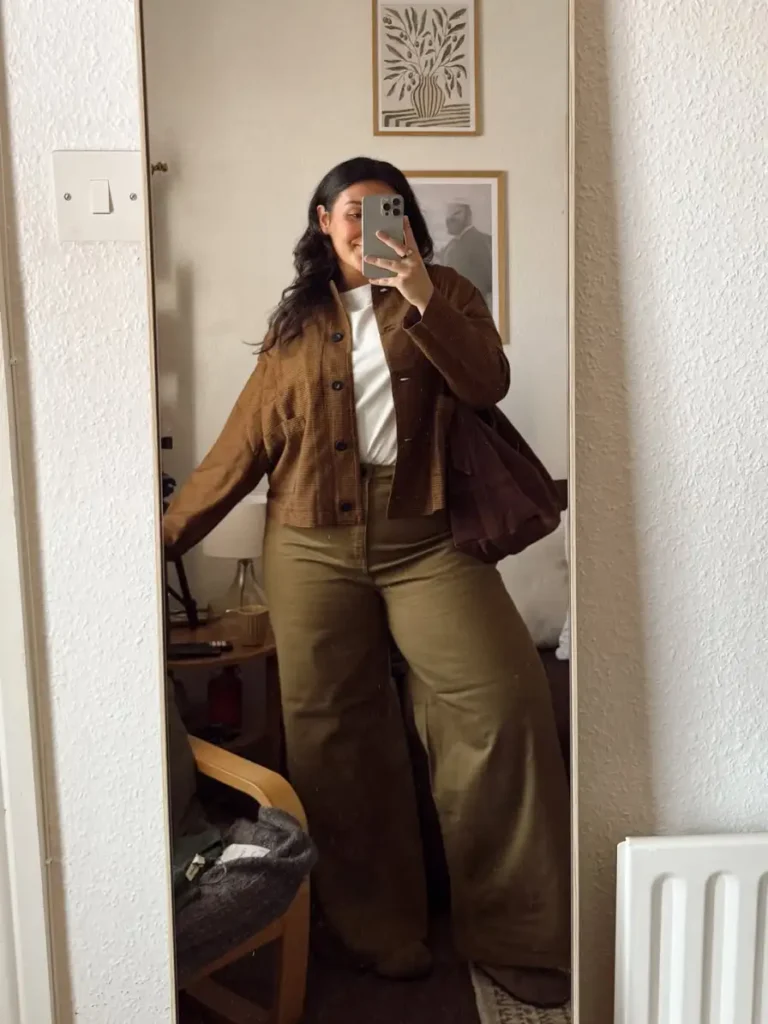 Plus size fall outfit with a brown corduroy jacket, white T-shirt, olive wide-leg trousers, and a dark brown shoulder bag.
